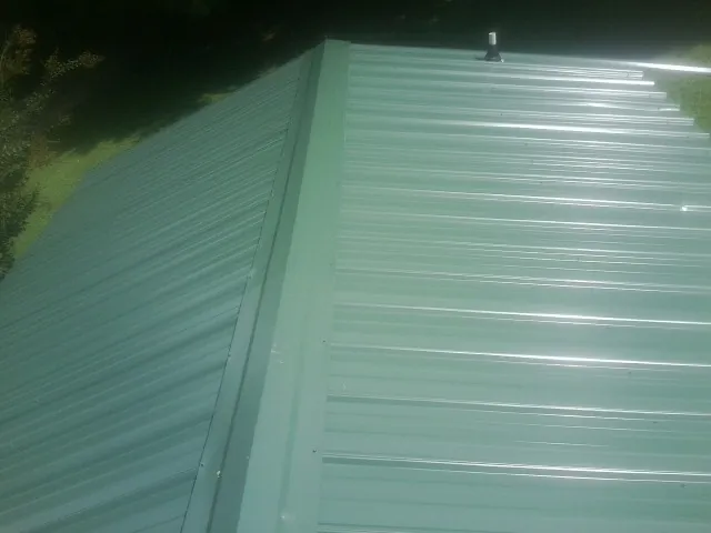 New green metal panels meeting at the ridge of a roof — Flat Roof Repair work by our crew in Pembroke Pines