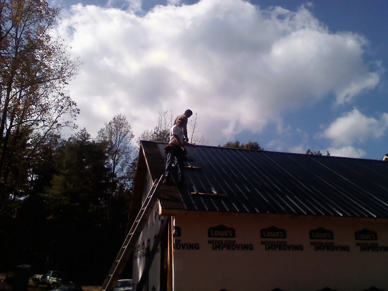 Roofer fastening dark metal panels high against a cloudy sky, from a Roof Inspection job in Pembroke Pines