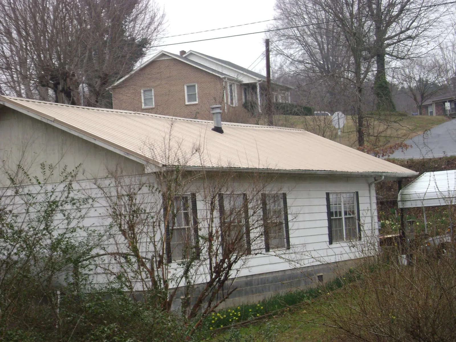 Tan metal roof on a white sided house set into a hillside — Commercial Roofing by Roofing Brothers in Pembroke Pines